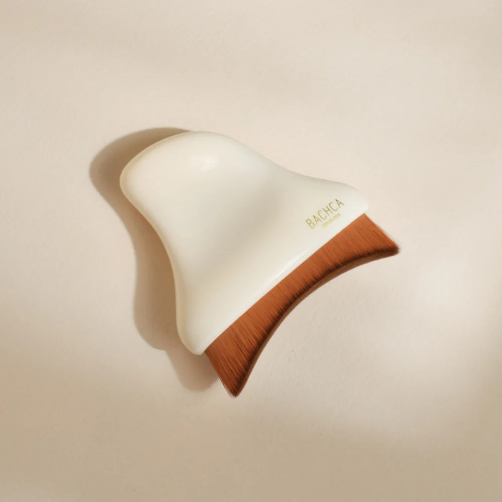Brosse visage Bachca en fibres fines, forme ergonomique pour massage du visage sur fond neutre.